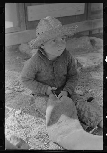 Little boy cutting up inner tube, El Indio, Texas