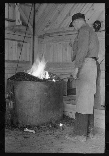 Blacksmith heating iron in forge, Southern Paper Mill construction shed, Lufkin, Texas