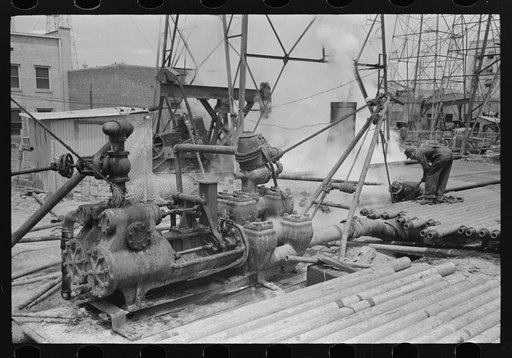Oil field workers working in the sluch pit; mud hog in left foreground, Kilgore, Texas