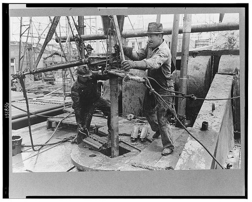 Oil field workers adding a length of pipe to drill stream by means of heavy pipe wrenches, Kilgore, Texas
