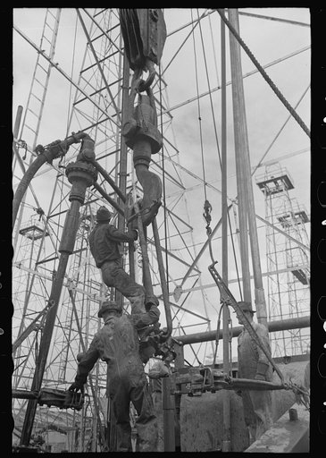 Activity at oil well; man on lengths of traveling block will be pulled up to the crown block at top of derrick, Kilgore, Texas