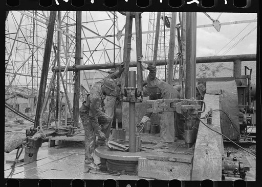 Removing length of pipe from oil well, Kilgore, Texas. Clamps being removed from rotary table and pipe will be elevated by the links and clamp of the elevator