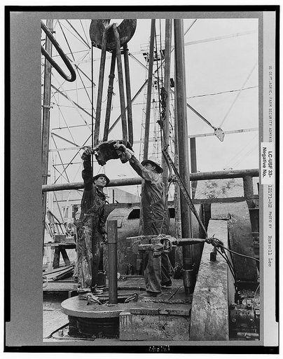Oil field workers, reaching for clamp on elevator. The elevator removes the pipe from the drill hole, Kilgore, Texas