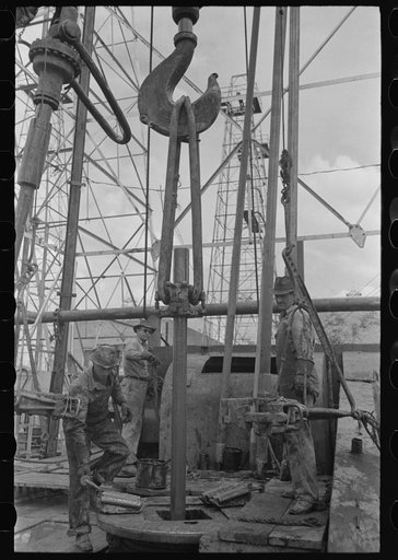 Untitled photo, possibly related to: Oil field workers, reaching for clamp on elevator. The elevator removes the pipe from the drill hole, Kilgore, Texas