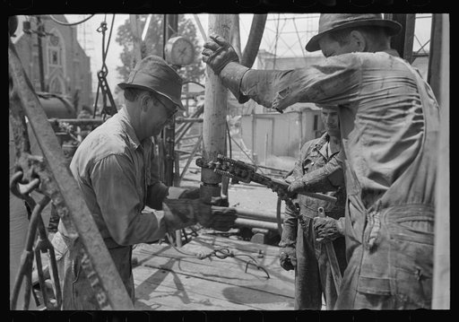 Oil field worker screwing nipple on end of drill stem for test to determine direction and draft of drilling operations, Kilgore, Texas