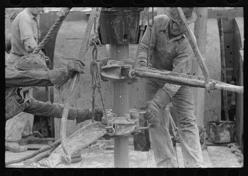 Oil field workers releasing pipe wrenches from drill pipe, oil well, Kilgore, Texas