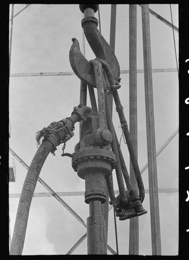 Detail of oil drilling equipment: hook of the traveling block, links and clamp of the elevator, hose connection from mud hog and swivel. Oil well, Kilgore, Texas