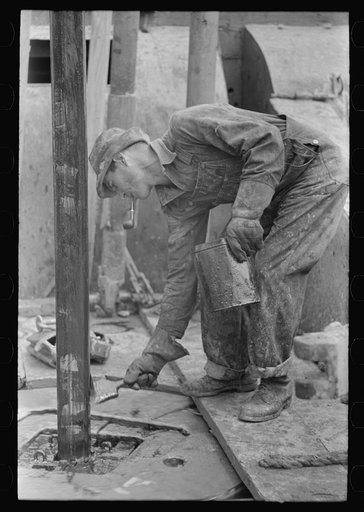 Oil field worker applying grease to rotating drill pipe, Kilgore, Texas
