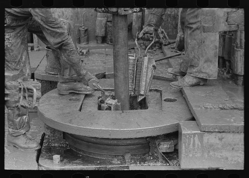 Untitled photo, possibly related to: Removing clamps from rotary tacle before lifting out drilling pipe, oil well, Kilgore, Texas