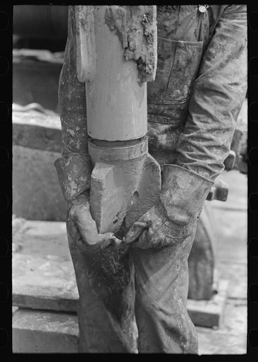 Screwing on the bit. Hole through which mud is forced from the mud hog may be seen in the bit. Oil well, Kilgore, Texas