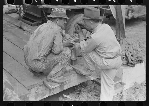 Untitled photo, possibly related to: Oil field workers squatting down while talking to bit salesman, Kilgore, Texas