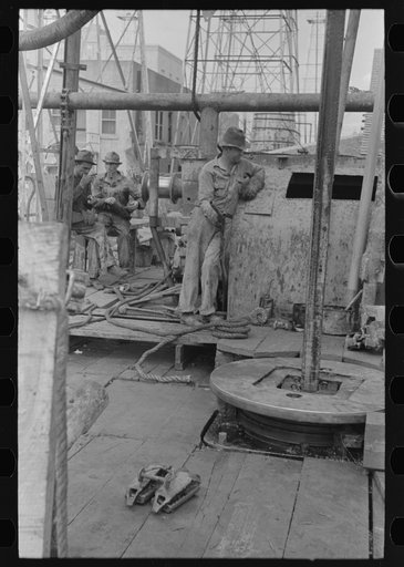 Untitled photo, possibly related to: Oil drillers talking with bits in front of them and drilling equipment in background, Kilgore, Texas