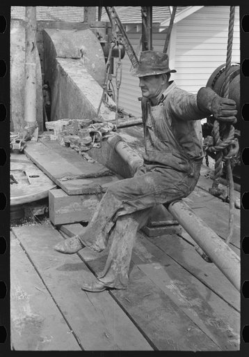Oil field worker resting on a length of pipe, Kilgore, Texas