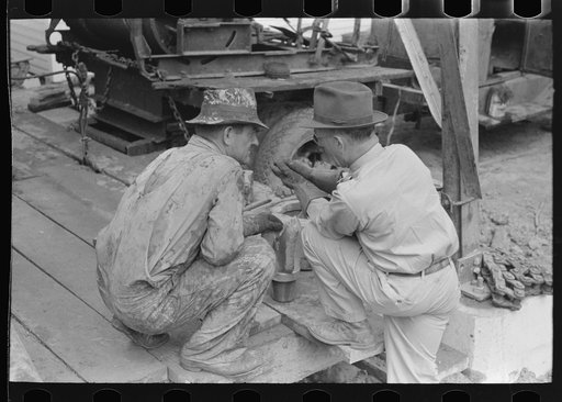 Oil field workers squatting down while talking to bit salesman, Kilgore, Texas