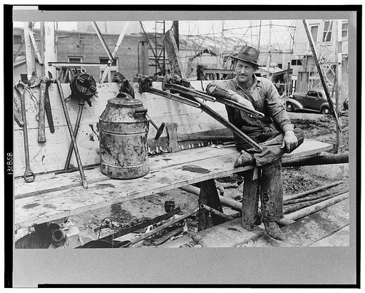 Oil field worker resting on pipe wrench, Kilgore, Texas