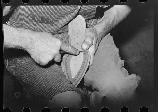 Punching holes in welt with awl to facilitate sewing of uppers to sole. Bootmaking shop, Alpine, Texas