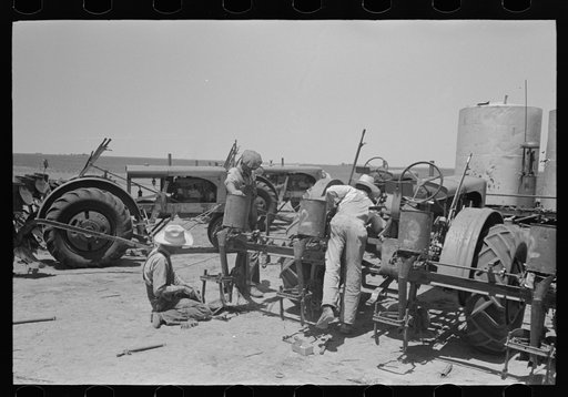 Day laborer changing plow points on tractor-drawn four-row planter. Gasoline tanks in the background, large farm near Ralls, Texas