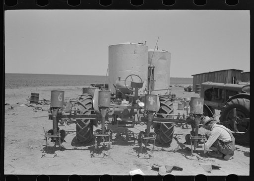 Day laborer changing plow points on tractor-drawn four-row planter. Gasoline tanks in the background, large farm near Ralls, Texas