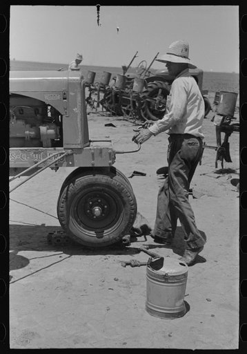 Day laborer cranking tractor on farm near Ralls, Texas