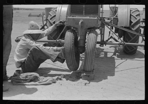 Day laborer pushing wheel onto tractor, large farm near Ralls, Texas