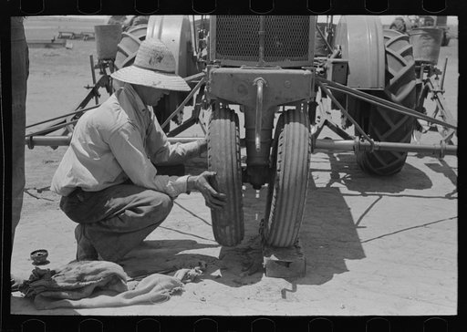 Day laborer putting front wheel onto tractor, large farm near Ralls, Texas