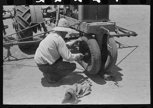 Day laborer tightening bearing on front wheel of tractor, farm near Ralls, Texas