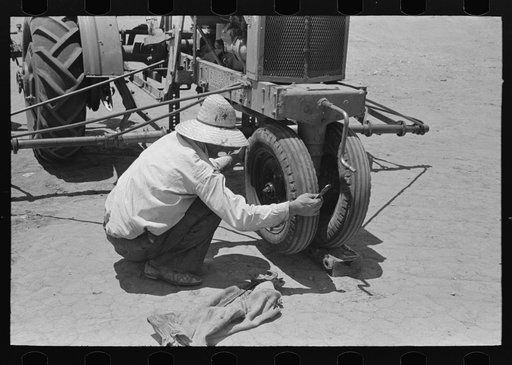Day laborer testing play on front wheel bearing of tractor, farm near Ralls, Texas