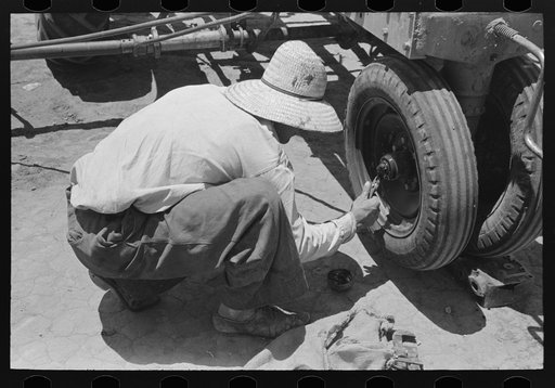 Day laborer putting in cotter pin in front of tractor, farm near Ralls, Texas