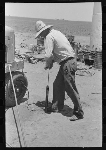 Day laborer pumping up tractor tire, farm near Ralls, Texas