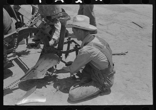 Day laborer adjusting plow points on tractor-drawn planter, farm near Ralls, Texas