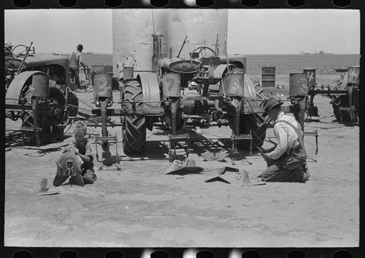 Day laborer adjusting plow points on tractor-drawn planter, farm near Ralls, Texas