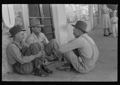 Farmers sitting against wall and squatting on sidewalk, Spur, Texas