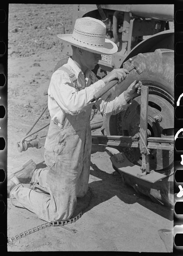Day laborer repairing link of chain which operates planter feed, farm near Ralls, Texas