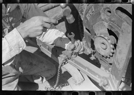 Day laborer repairing link of chain which operates planter feed, farm near Ralls, Texas