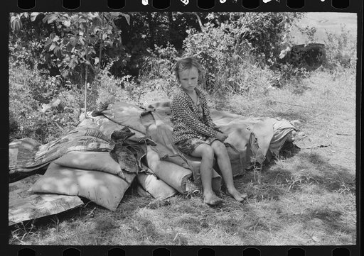 Child of family encamped by the roadside sitting on bedclothing.  There were no beds and no overhead covering near Spiro. Sequoyah County, Oklahoma