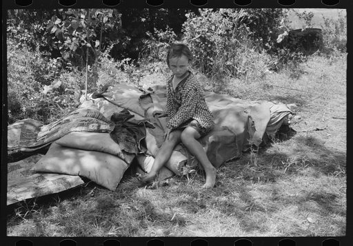 Child of agricultural day laborers camped near Spiro, Oklahoma. She is sitting on the bedroll. There was no bed in the camp. Sequoyah County, Oklahoma