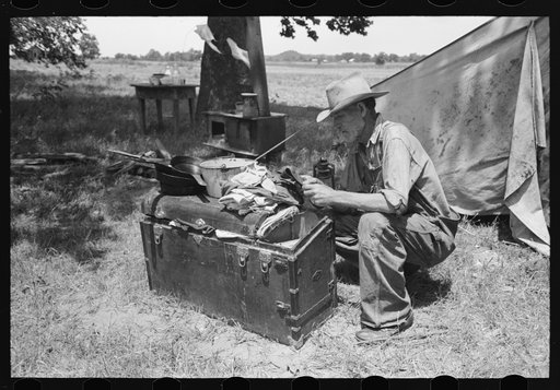 Veteran migrant agricultural worker examining contents of his trunk, camped on Arkansas River in Wagoner County, Oklahoma