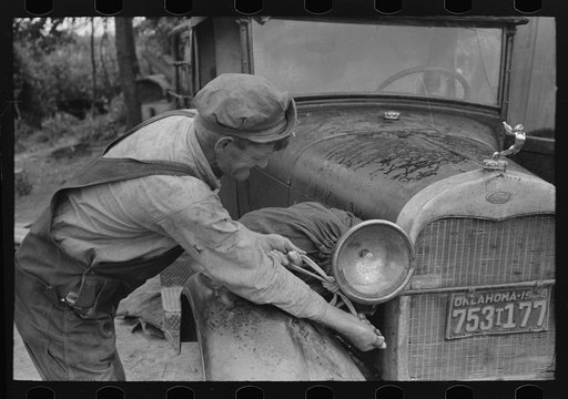 Elmer Thomas, migrant to California, tying sack of laundry onto front lamp bracket near Muskogee, Oklahoma