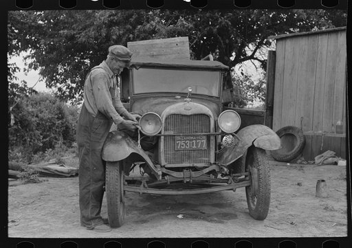 Untitled photo, possibly related to: Elmer Thomas, migrant to California, tying sack of laundry onto front lamp bracket near Muskogee, Oklahoma