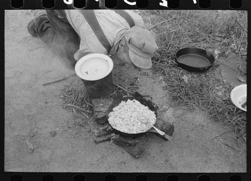 Nursing along the fire by blowing on it. Potatoes are being cooked in this pan. Migrant family en route to California near Henrietta [i.e., Henryetta,] Oklahoma