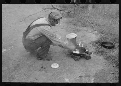 Elmer Thomas putting lard into the frying pan. At roadside camps each person in a migrant camp has his own duties. In this case, Mr. Thomas is attending the fire. There are a certain number of assignments which have been given him, of which this is one. Near Henrietta [i.e., Henryetta,] Oklahoma