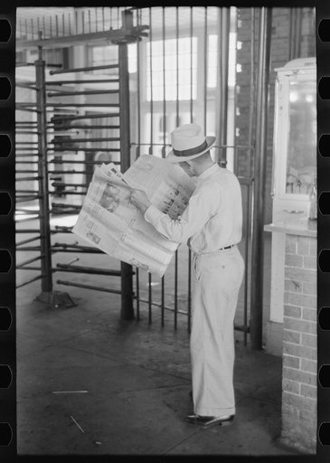 Man reading newspaper while waiting for streetcar. Streetcar station, Oklahoma City, Oklahoma