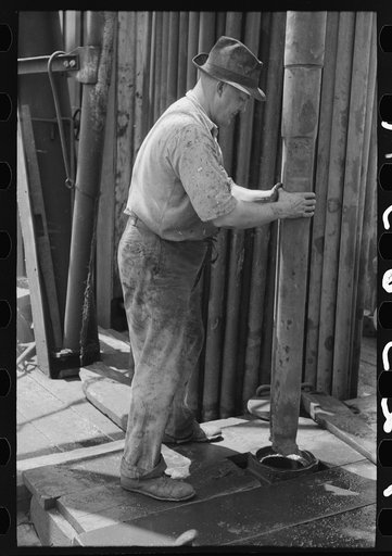 Roughneck guiding bailer into hole during bailing out operations, oil well near Seminole, Oklahoma. They were bailing out mud and water in old well before drilling to a deeper level