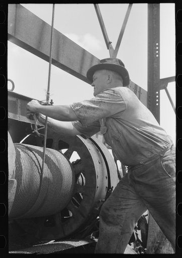 Roughneck tying piece of string around cable to determine depth to which bailer is being lowered. Oil well near Seminole, Oklahoma