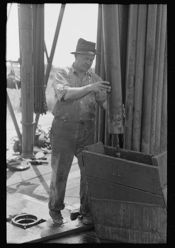 Untitled photo, possibly related to: Roughneck guiding bailer into hole during bailing out operations, oil well near Seminole, Oklahoma. They were bailing out mud and water in old well before drilling to a deeper level