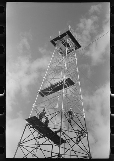 Painting a derrick, Seminole oil field, Oklahoma. Notice lack of safety belts. Painters say that safety devices slow them down too much