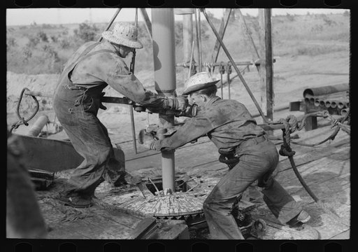 Adding a length of drilling pipe at oil well in Seminole oil field, Oklahoma. Wrenches applied to loosen pipe