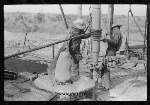 Adding a length of drilling pipe at oil well in Seminole oil field, Oklahoma. Lower end of traveling block is attached to pipe in rat hole by means of rope operated off winch