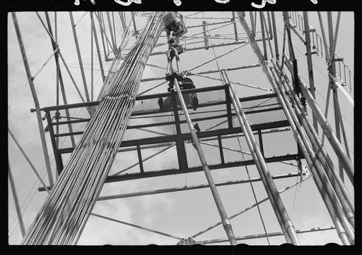 Untitled photo, possibly related to: Looking up in an oil derrick. Roughneck inserting lengths of pipe into the elevator for pulling the casings. Oklahoma City, Oklahoma