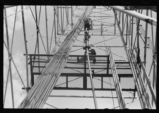 Looking up in an oil derrick. Roughneck inserting lengths of pipe into the elevator for pulling the casings. Oklahoma City, Oklahoma